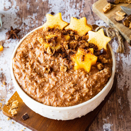 Lebkuchen-Porridge in einer weißen Schüssel serviert und mit Khaki (in Sternform ausgestocken) und mit Lebkuchenbröseln dekoriert.
