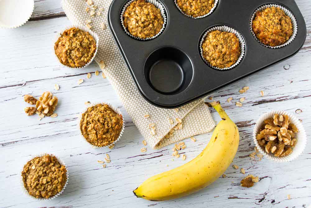 Bananen-Walnuss-Muffins in einem Muffinsblech, manche liegen auch daneben, sowie eine Banane.