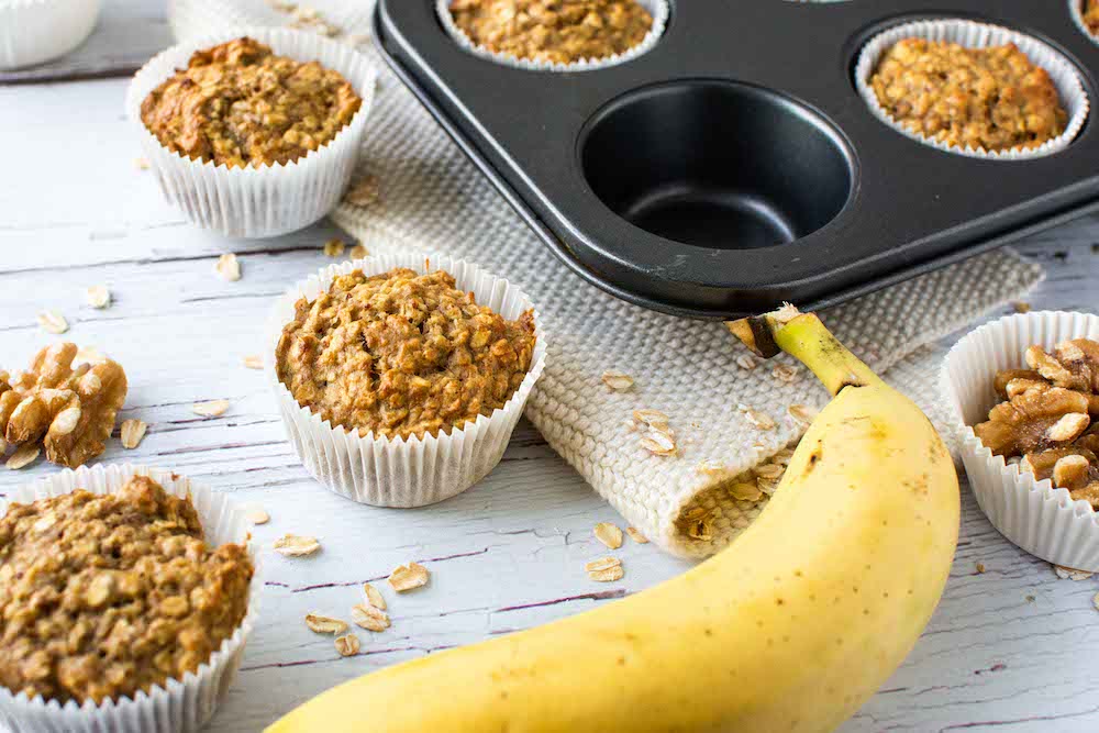 Bananen-Walnuss-Muffins, die teilweise in einem Muffinsblech und teilweise daneben liegen. 