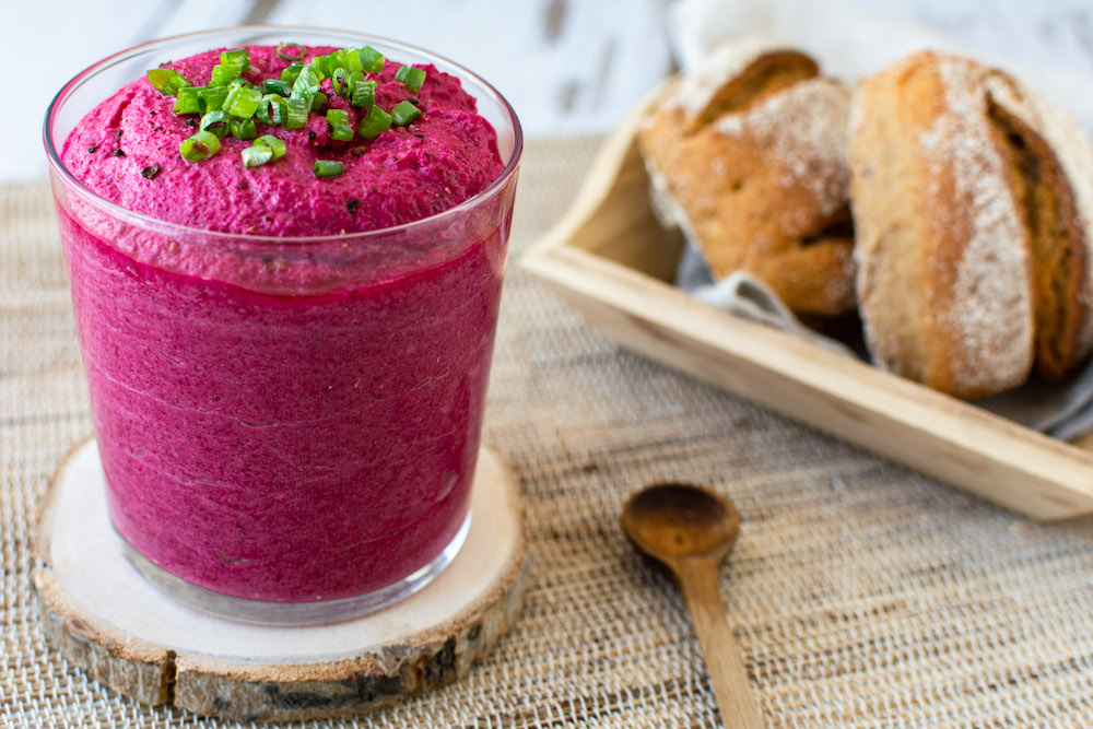 Intensiv gefärbter Dip aus roter Bete und Feta in einem Glas serviert und mit Frühlingszwiebeln bestreut.