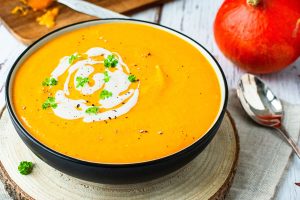 Kürbis-Süßkartoffel-Suppe in einer Schüssel serviert, mit Joghurt und Petersilie dekoriert.