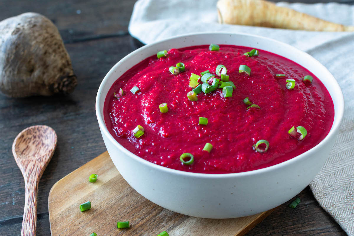 Rote Bete-Pastinaken-Suppe in einer Schüssel serviert und mit Frühlingszwiebeln bestreut.