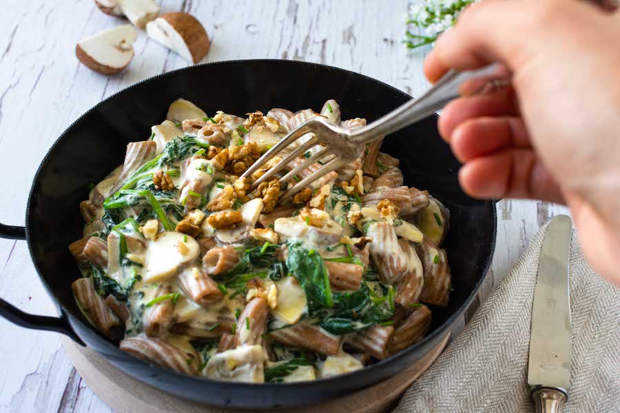 Vegane One Pot Pasta mit Spinat und Champignons in einer schwarzen Pfanne serviert