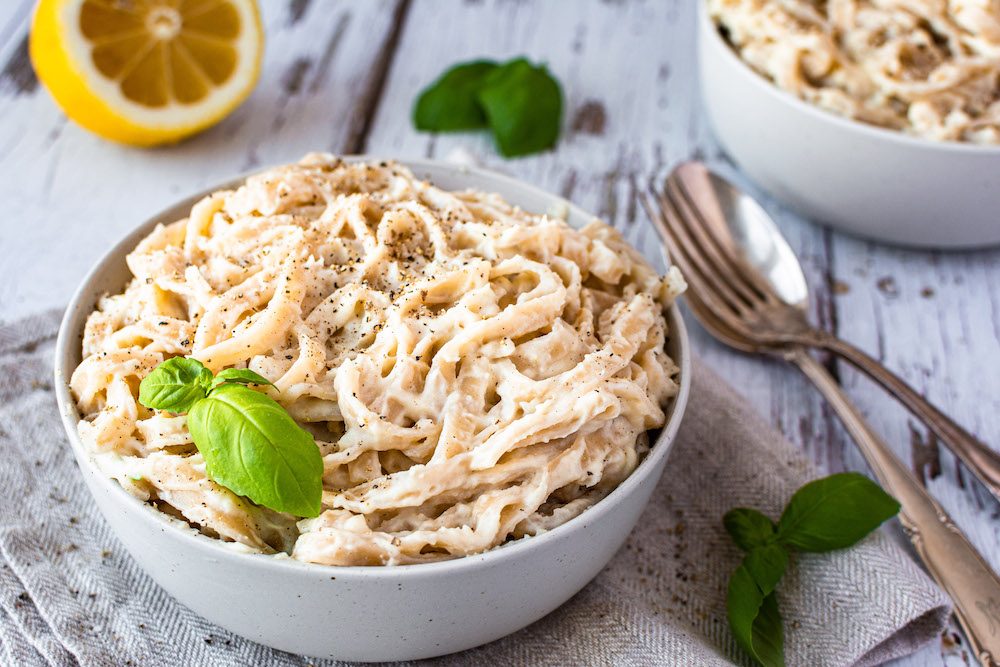 Blumenkohl Nudelsauce gesund vegan Rezept Linguine mit einer cremigen Blumenkohl-Nudelsauce vermengt, in einer Schüssel serviert und mit einem Basilikum-Blatt dekoriert.