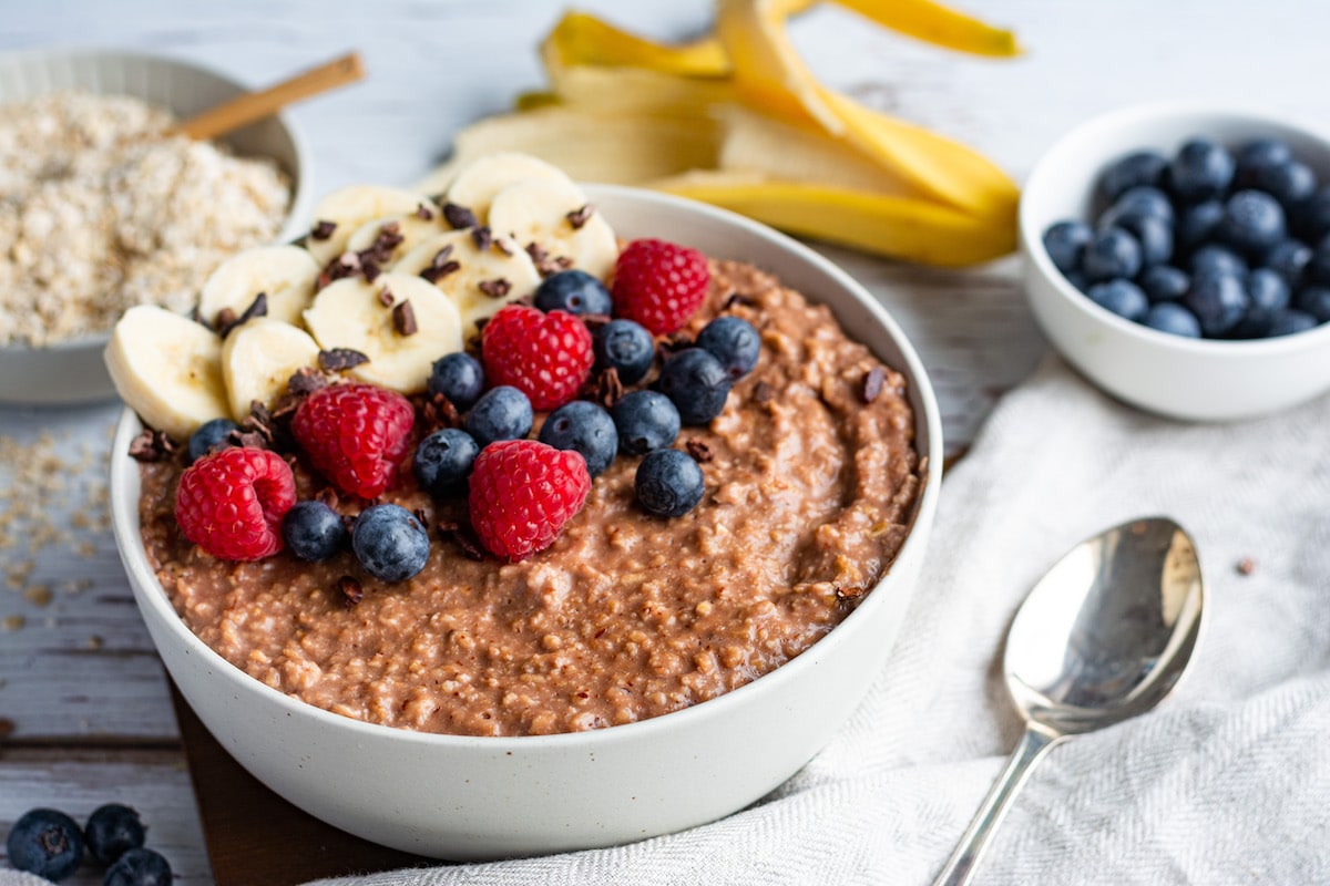 Kakao-Porridge in einer weißen Schüssel serviert und mit Bananen, Beeren und Kakaonibs dekoriert.