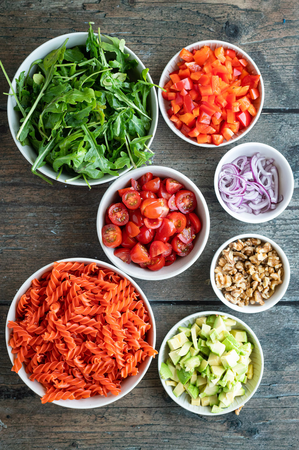 Zutaten für den Linsennudelsalat in Schüsseln: Rote Linsen Pasta, Rucola, rote Paprika, Cherrytomaten, Zwiebeln, Walnüsse, Avocado.