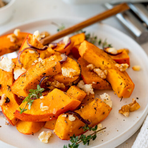 Ofenkürbis mit Feta, Walnüssen, Thymian und Zwiebeln auf einem weißen Teller serviert.