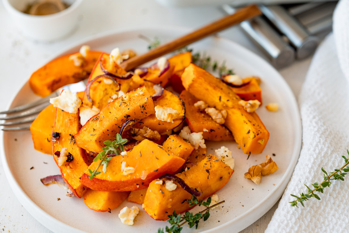 Ofenkürbis mit Feta, Walnüssen, Thymian und Zwiebeln auf einem weißen Teller serviert.