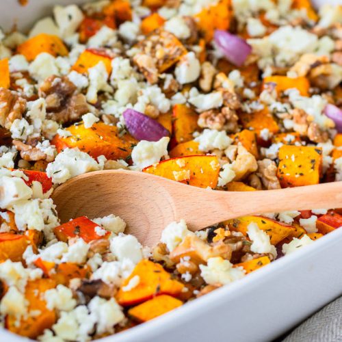 Ofenkürbis mit Feta und Walnüssen in einer weißen Auflaufform mit einem Holzlöffel.