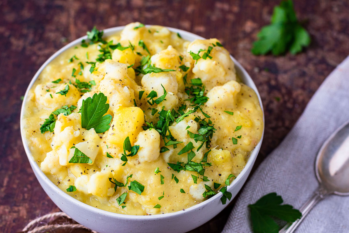 Blumenkohl-Kartoffel-Curry in einer weißen Schüssel serviert und mit Petersilie dekoriert.