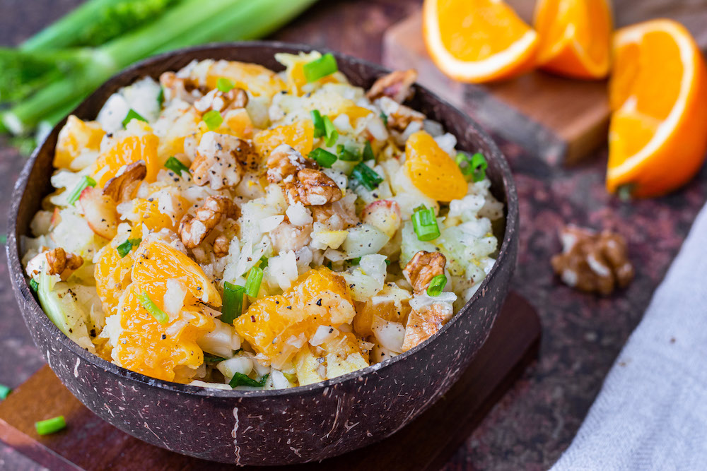 Rohkost-Salat mit Fenchel und Orangen in einer Kokosnuss-Schüssel serviert und mit Frühlingszwiebeln bestreut.