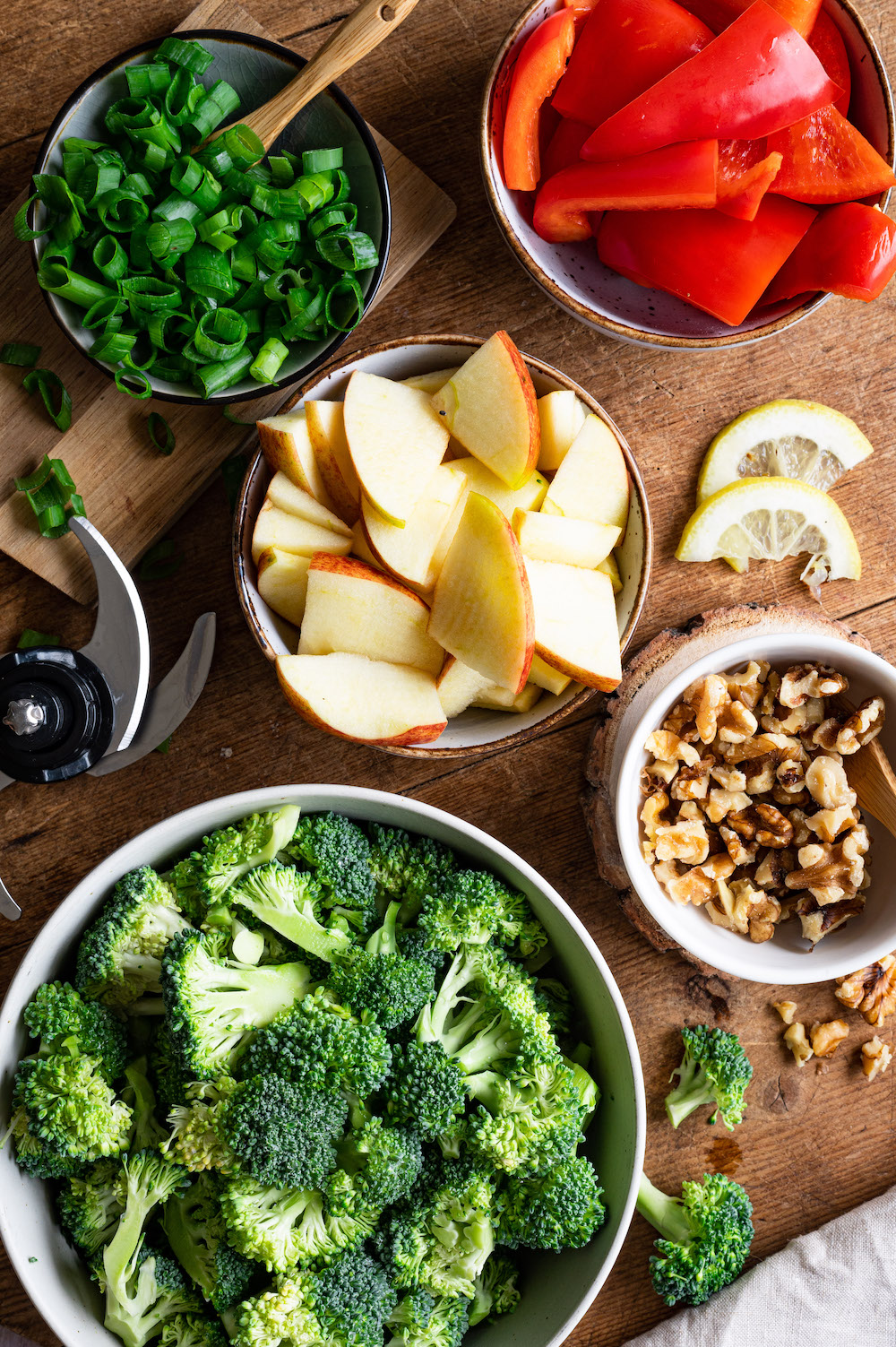Zutaten für Brokkoli-Salat in kleinen Schüsselchen arrangiert: Brokkoli, Apfel, Paprika, Walnüsse, Frühlingszwiebeln.
