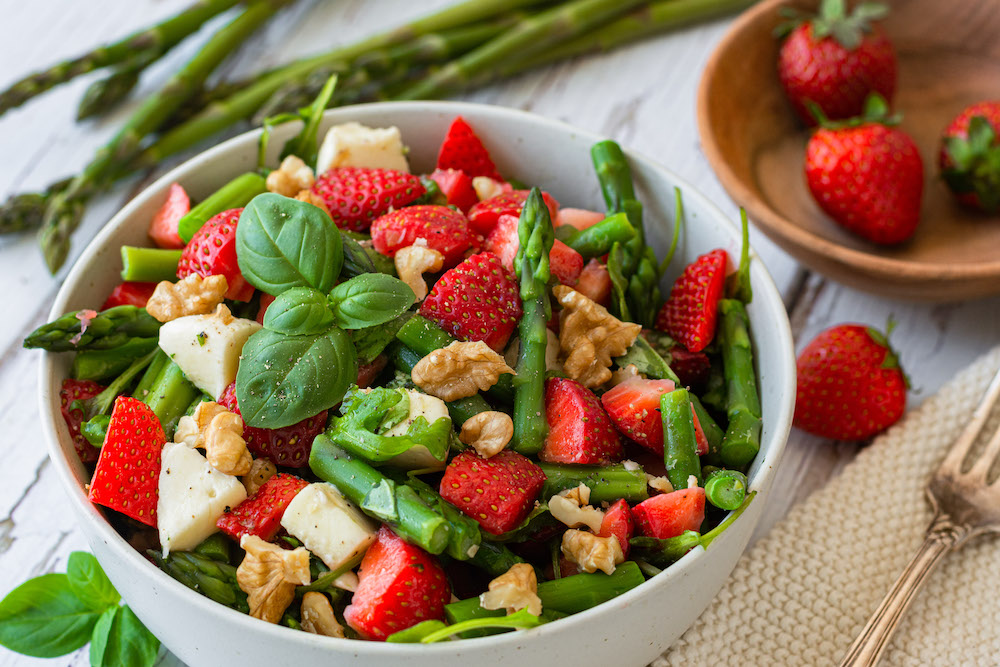 Schüssel gefüllt mit Salat aus grünem Spargel, Erdbeeren, Rucola, Mozzarella und Walnüssen