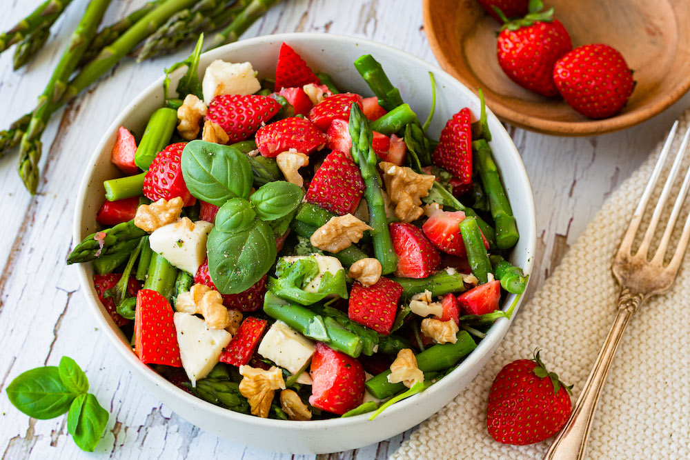 Spargel-Erdbeer-Salat in einer Schüssel, grüner Spargel und Erdbeeren im Hintergrund als Deko