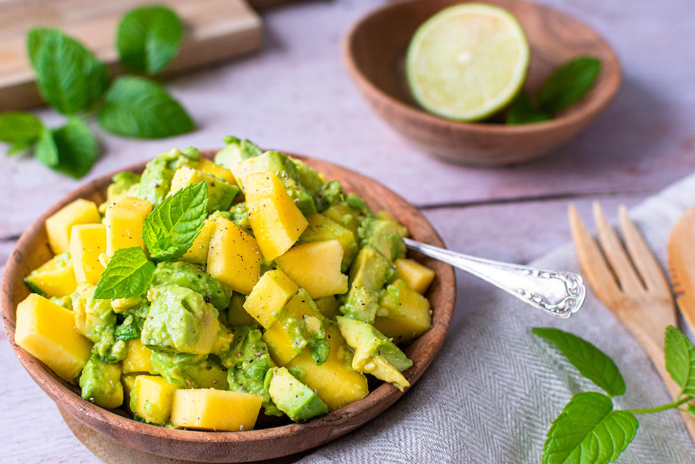 Avocado-Mango-Salat in einer Holzschüssel mit Minze dekoriert.