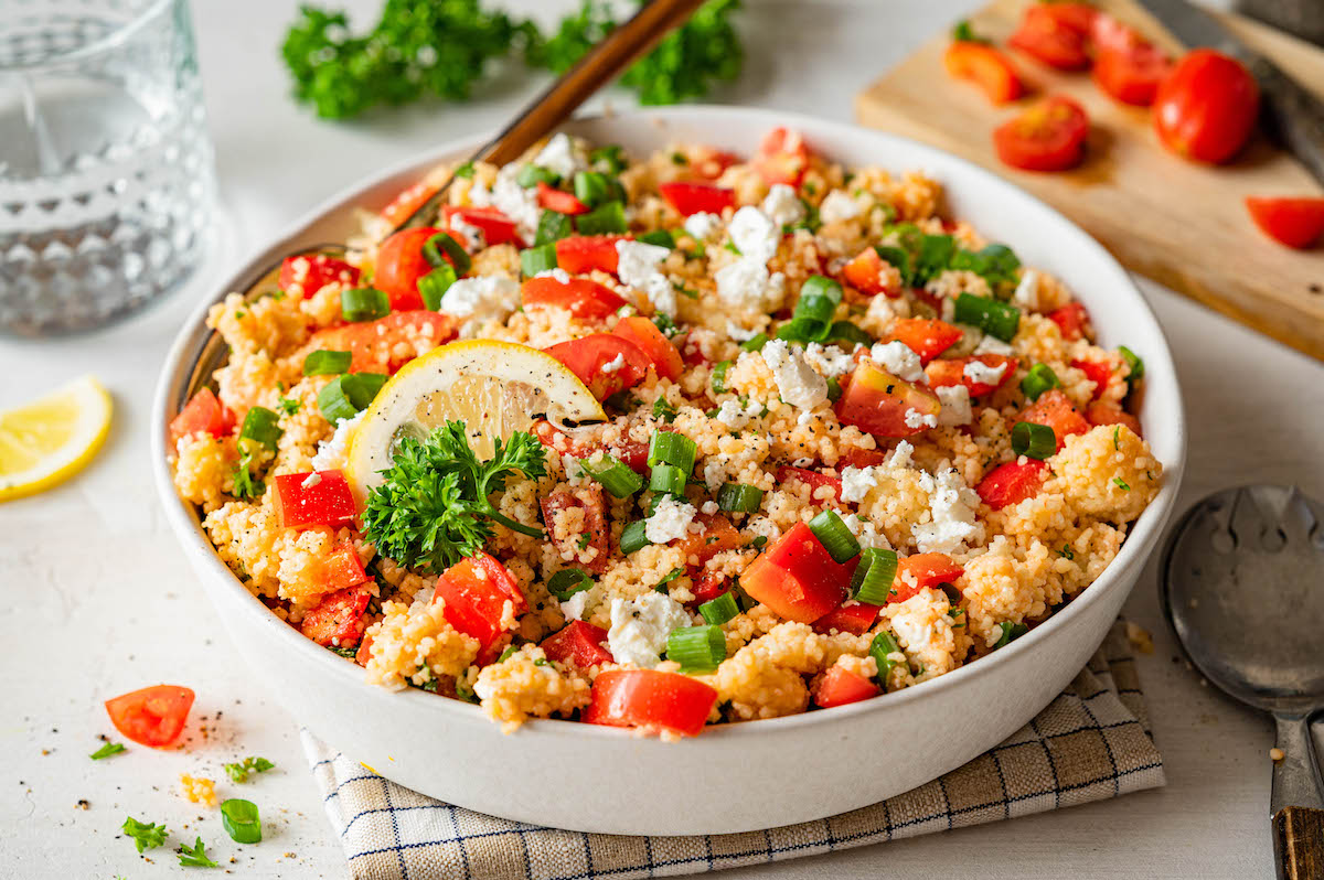 Couscous-Salat mit Feta, Paprika, Tomaten und Tomatenmark-Dressing in einer weißen Schüssel serviert.