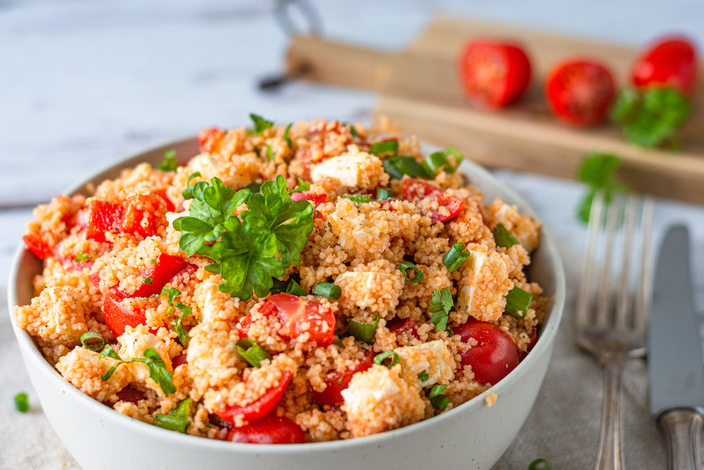 Couscous-Salat mit Tomate, Paprika und Feta in einer weißen Schüssel serviert.