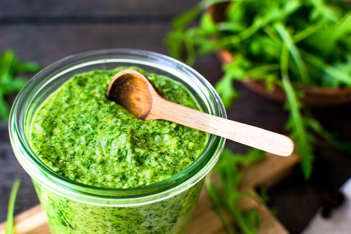 Grünes Rucola-Pesto in einem Glas mit einem kleinen Holzlöffel.