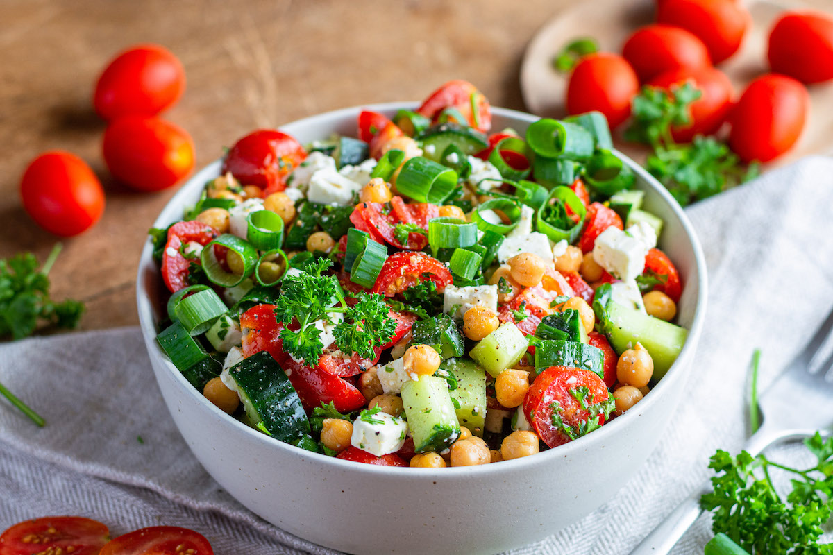 Kichererbsen-Feta-Salat mit Gurke und Tomaten in einer weißen Schüssel serviert.