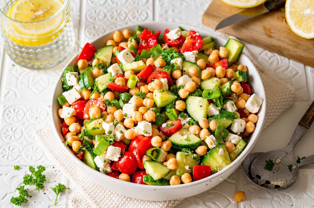 Kichererbsensalat mit Feta, Gurke und Tomate in einer weißen Schüssel.
