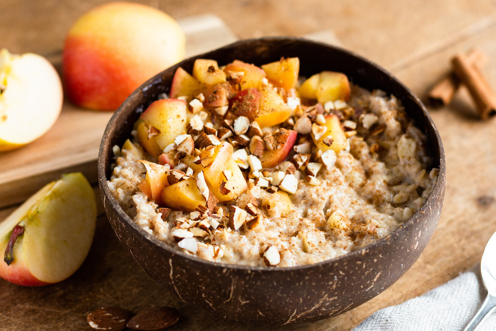 Apfel-Zimt-Porridge in einer Bambus-Schüssel serviert und mit Zimtäpfeln und Mandeln dekoriert.