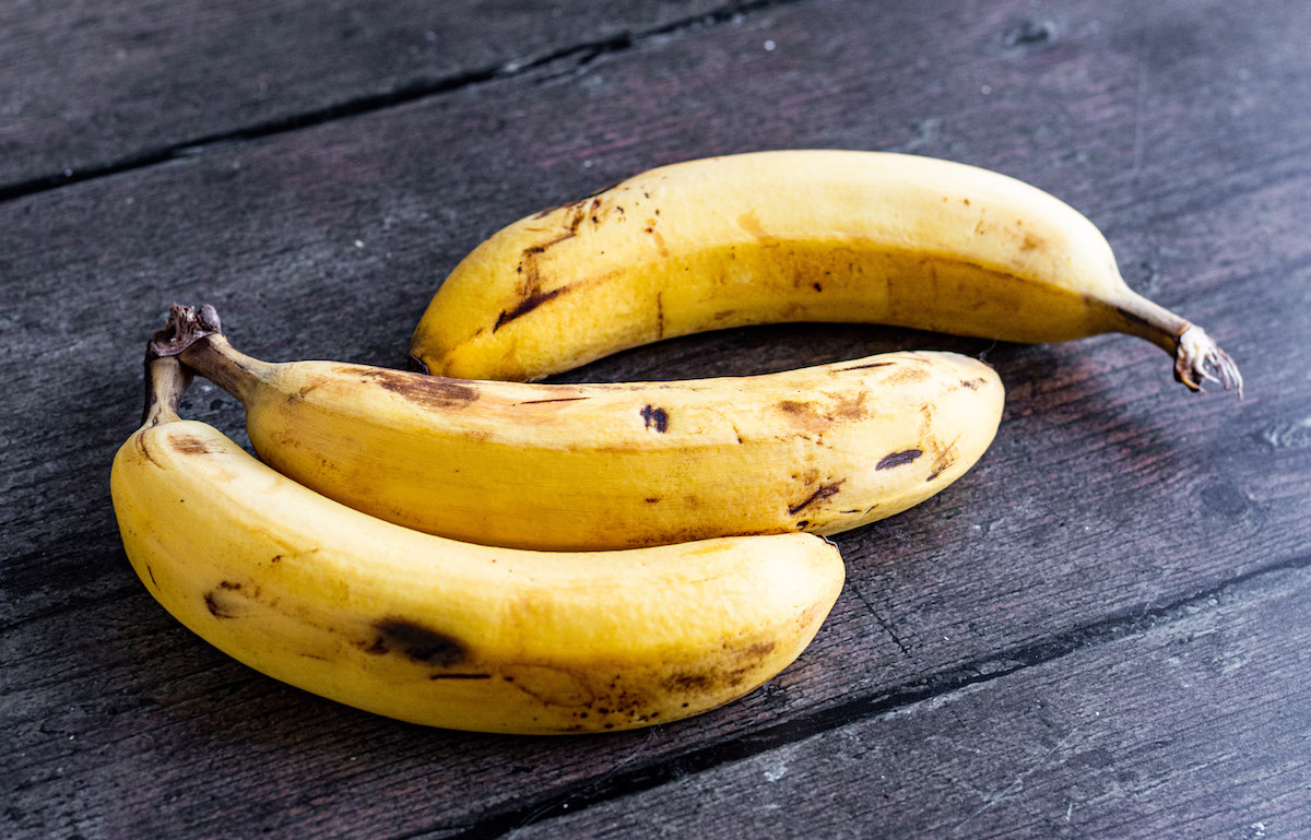 Drei reife, braune Bananen auf einem Holzuntergrund.