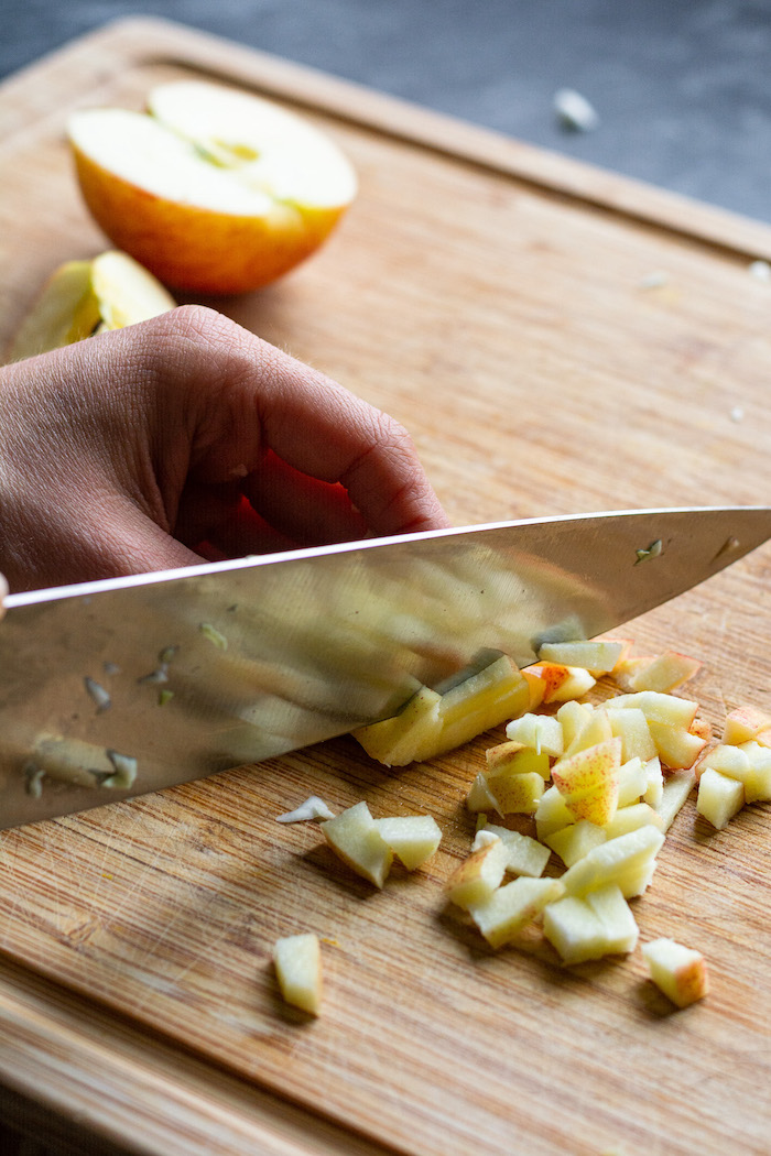 Geviertelte Äpfel auf einem Holzbrett, einer wird gerade mit einem Messer in kleine Stücke geschnitten.