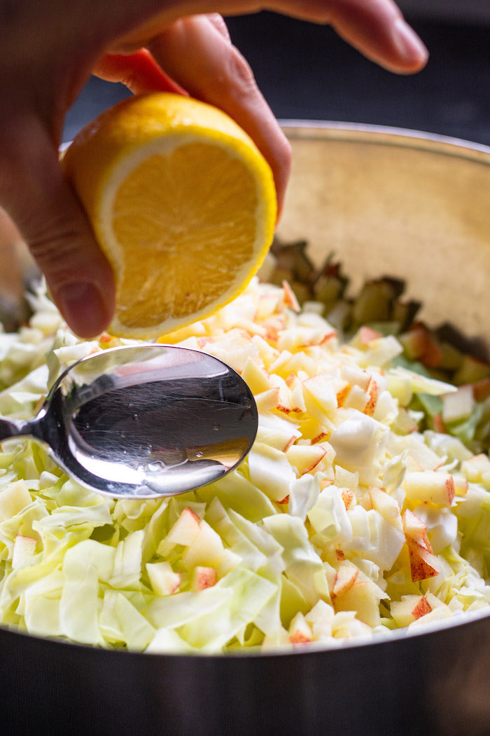 Spitzkohlsalat in einer Metallschüssel, über welchen gerade eine Zitrone für das Dressing ausgepresst wird.