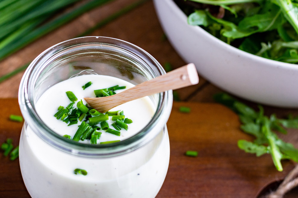 Joghurt-Dressing mit Senf und Honig in einem Glas mit einem Löffel serviert und mit Schnittlauch bestreut.