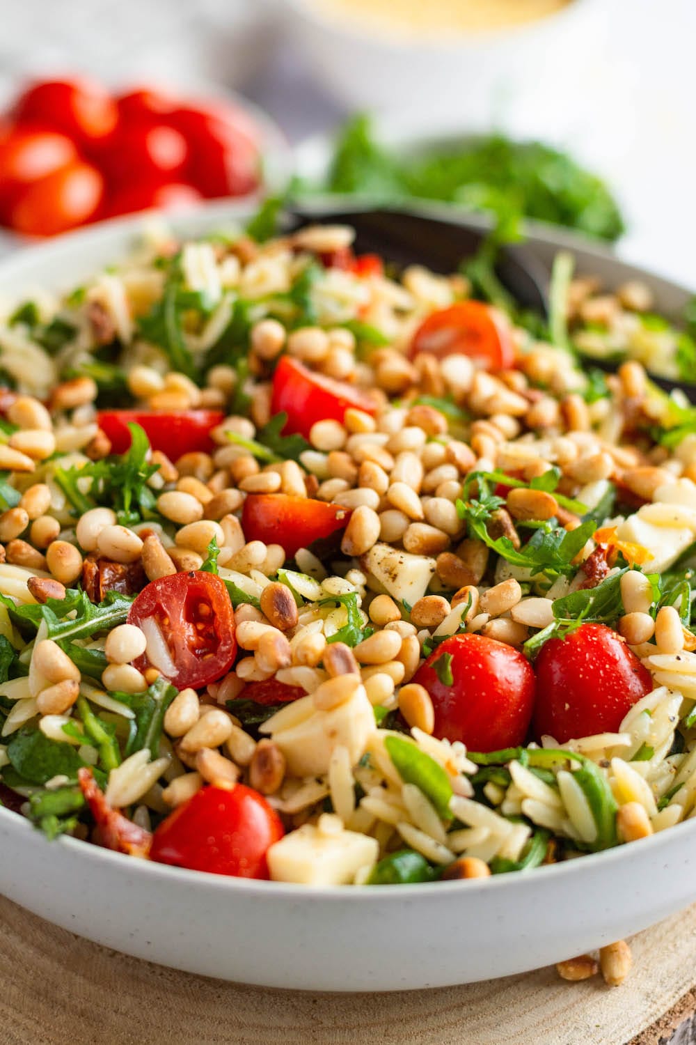 Nahaufnahme des Orzo-Salats in einer weißen Schüssel, welche auf einem Holzbrett steht.