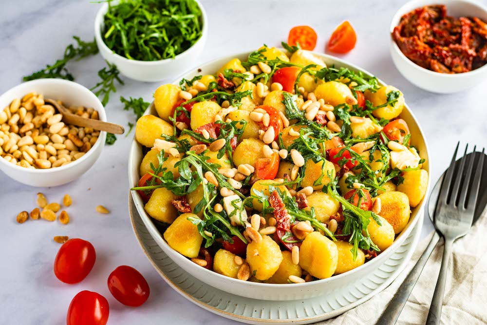 Gnocchi-Salat mit Rucola, Mozzarella und Tomaten in einer weißen Schüssel serviert.