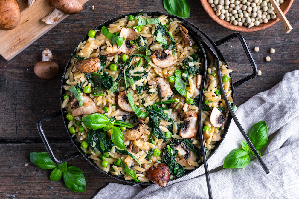 Pfannengericht mit Orzo-Pasta (Risoni), Spinat, Champignons und Erbsen in einer schwarzen Pfanne serviert.