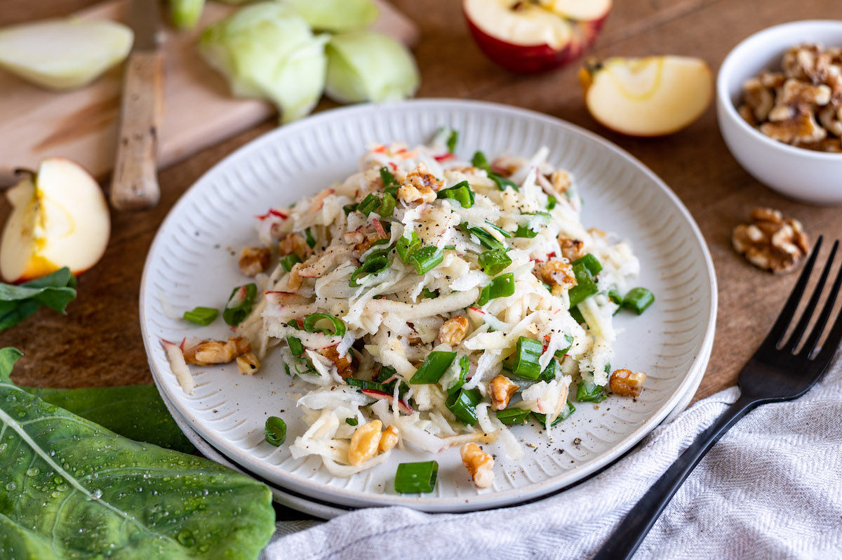 Geraspelter Kohlrabisalat mit Apfel, Frühlingszwiebeln und Walnüssen auf einem flachen Teller angerichtet.