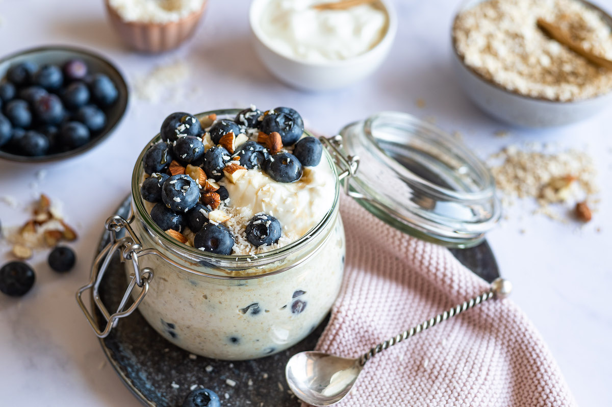 Overnight Oats mit Quark und Heidelbeeren in einem Schnappverschlussglas. Mit Heidelbeeren, gehackten Mandeln und Kokosraspeln dekoriert.