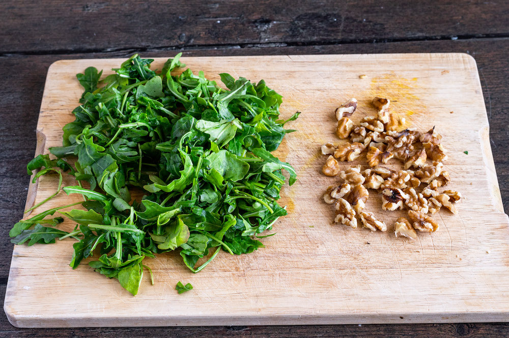 Schneidbrett mit klein gezupftem Rucola und zerbröselten Walnüssen.