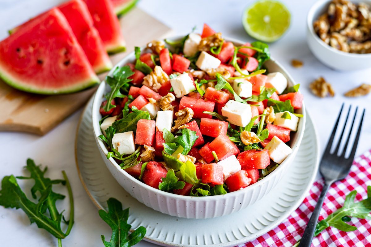 Wassermelonen-Feta-Salat mit Rucola Wassermelonen-Feta-Salat mit Rucola und Walnüssen in einer weißen Schüssel.