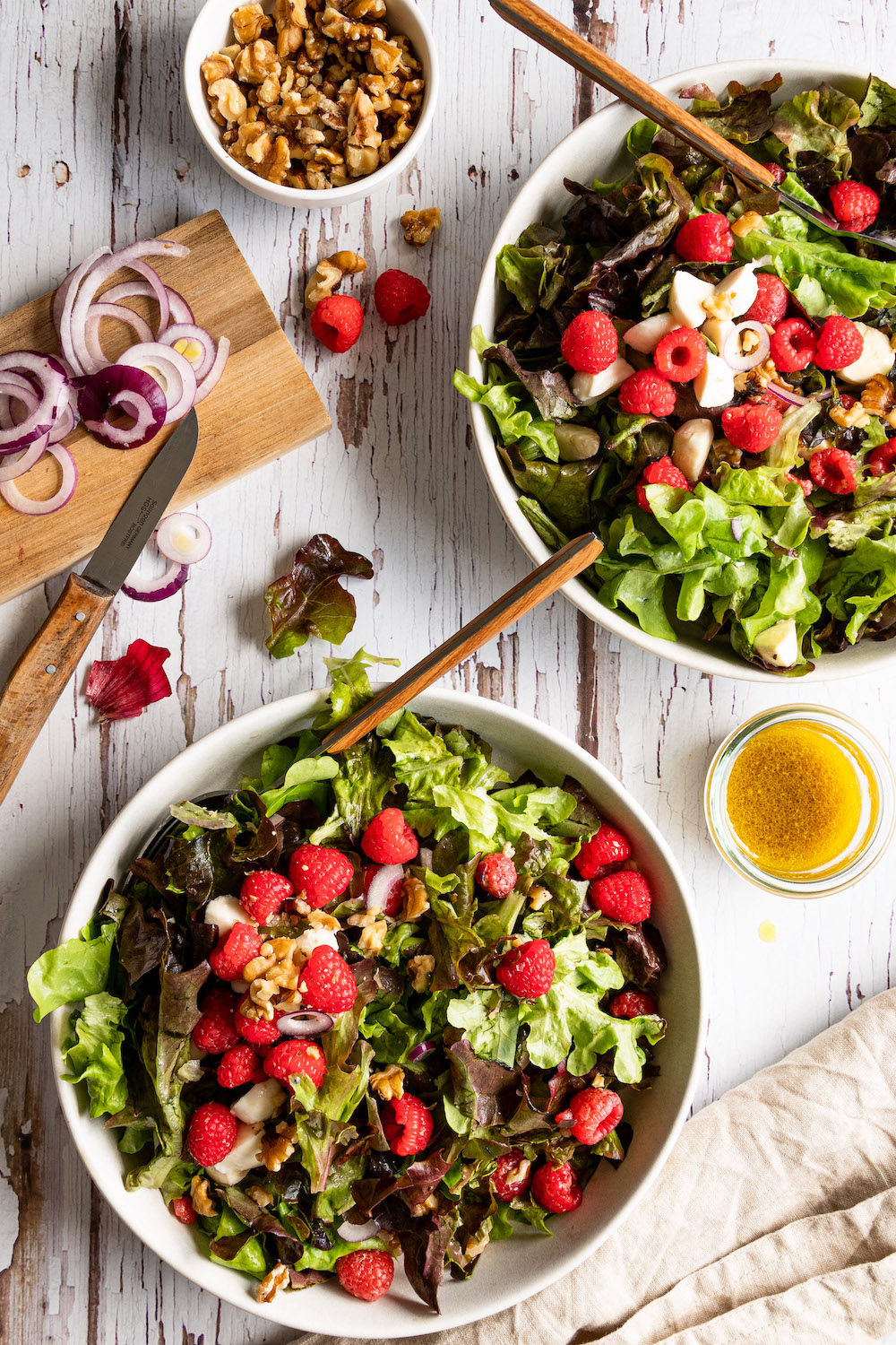 Zwei Schüsseln mit grünem Salat mit Himbeeren und Walnüssen. In jeder Schüssel steckt eine Gabel mit Holzgriff.