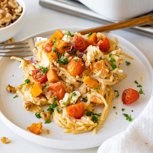 Kürbis-Feta-Pasta mit Tomaten, Walnüssen und Zwiebeln auf einem flachen Teller serviert.