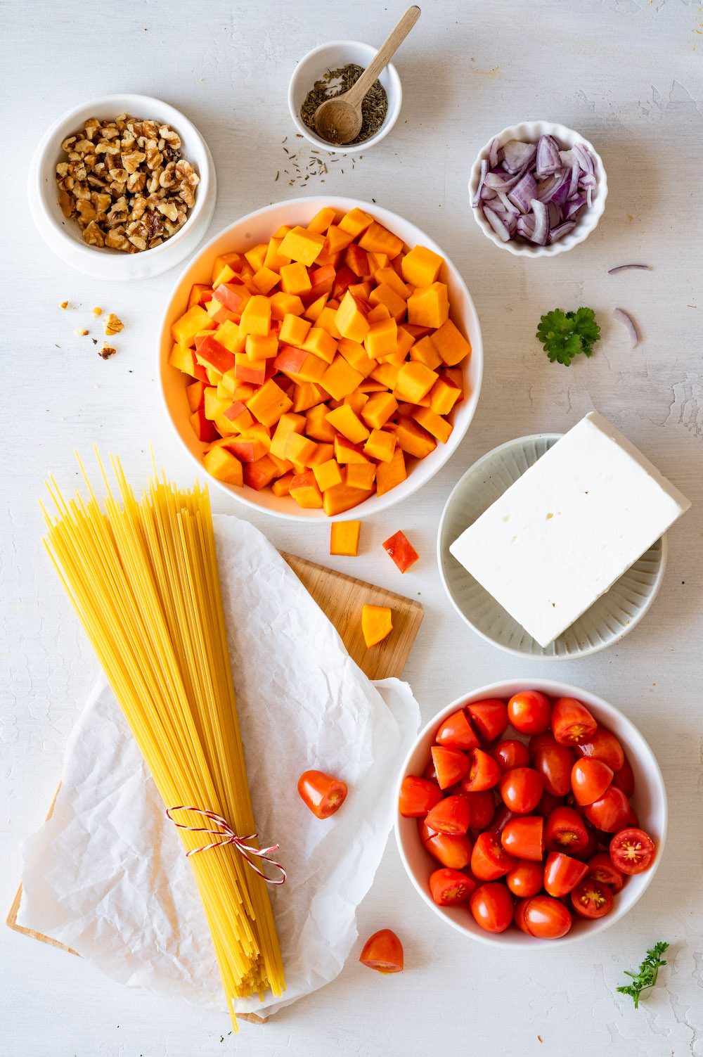 Zutaten für die Kürbis-Feta-Pasta aus der Vogelperspektive fotografiert: Spaghetti, Cherrytomaten, Hokkaidokürbis, Feta, Walnüsse, rote Zwiebeln und Thymian.