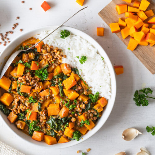 Kürbis-Linsen-Curry mit Spinat und Kokosmilch mit Reis in einer weißen Schüssel serviert.