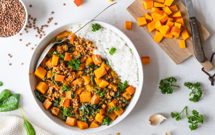 Kürbis-Linsen-Curry mit Spinat und Kokosmilch mit Reis in einer weißen Schüssel serviert.