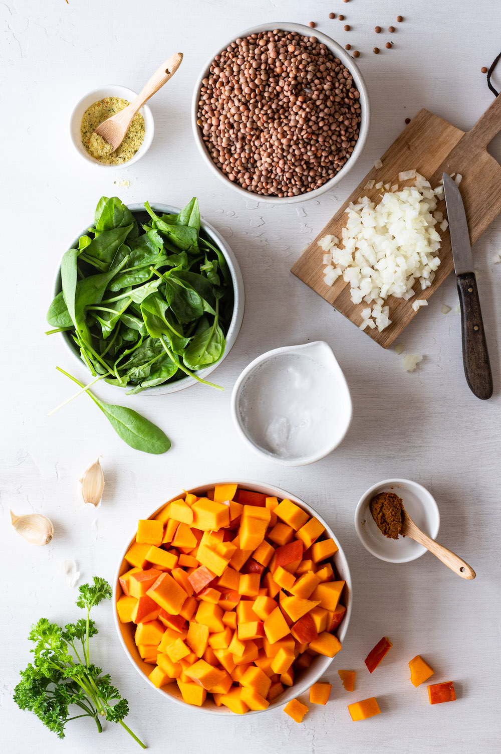 Zutaten für das Kürbis-Linsen-Curry aus der Vogelperspektive fotografiert: Hokkaido, Berglinsen, Spinat, Kokosmilch, Zwiebeln, Knoblauch, Gemüsebrühe, Currypaste und Petersilie.