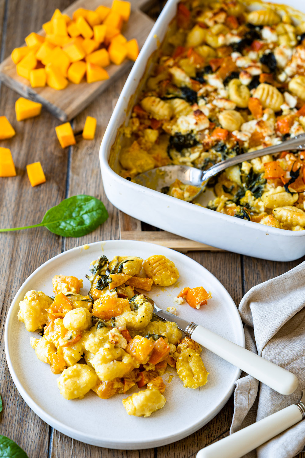 Kürbisauflauf mit Gnocchi, Spinat und Feta - eine Portion ist auf einem Teller serviert, im Hintergrund steht die Auflaufform, aus der dieser Teil fehlt.