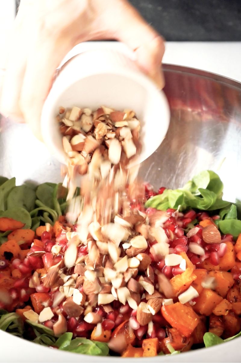 Mandeln werden in eine Schüssel geschüttet, in welcher sich bereits Feldsalat, Kürbis und Granatapfel befinden.