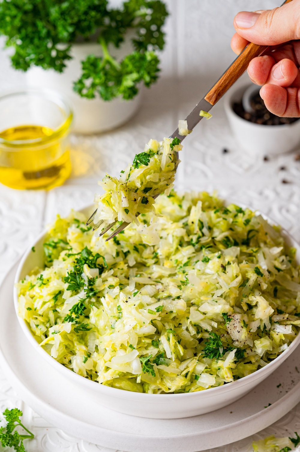 Krautsalat aus Spitzkohl, mit Zwiebeln und Petersilie verfeinert. In einer Schüssel serviert. Von oben wird mit einer Gabel gerade ein Bissen weggenommen.