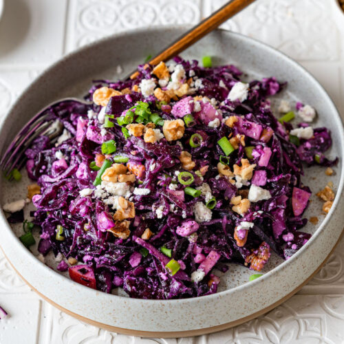 Rotkohlsalat mit Feta, Walnüssen und Apfel in einer grauen Schüssel serviert und mit Frühlingszwiebeln bestreut.