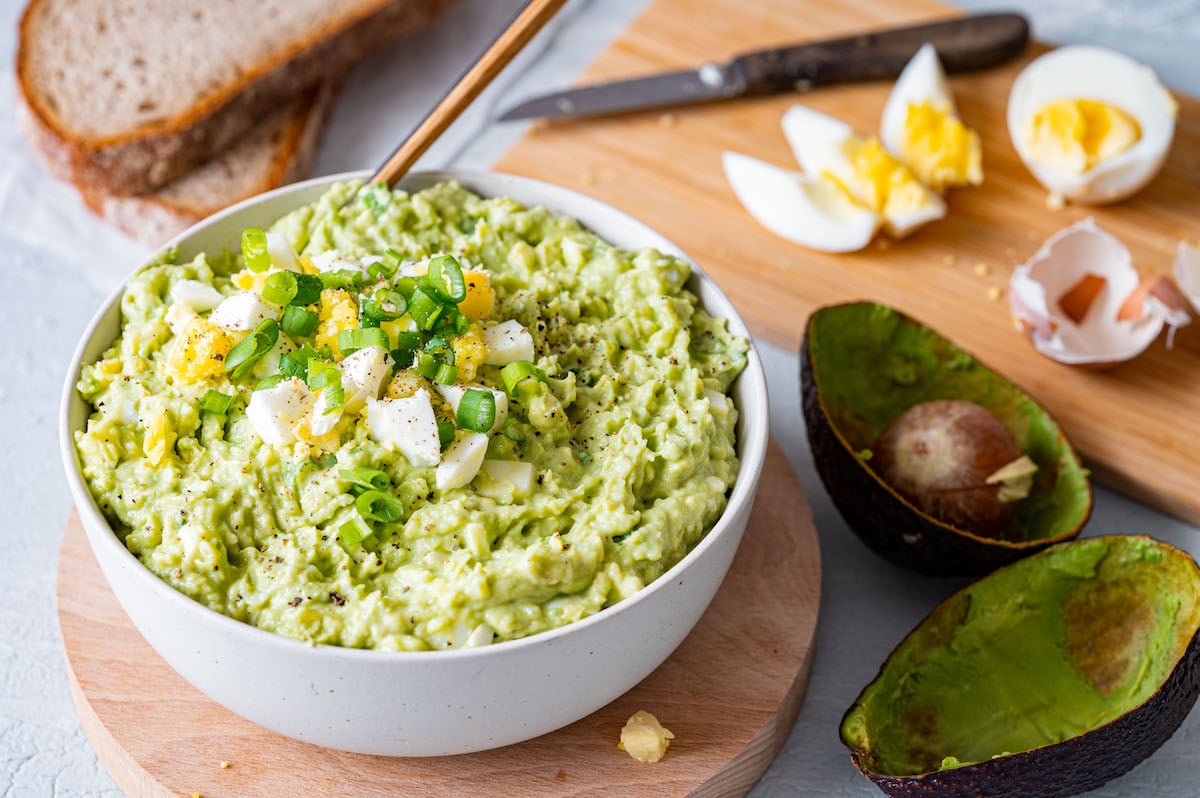 Avocado-Eier-Salat in einer weißen Schüssel serviert und mit gekochten Eiern, Frühlingszwiebeln und Pfeffer dekoriert.