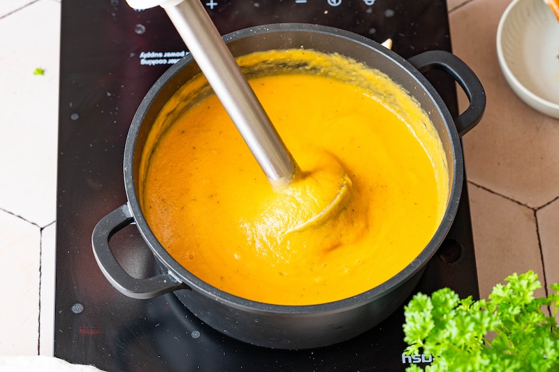 Pürierte Süßkartoffel-Linsen-Suppe in einem schwarzen Topf mit Pürierstab.