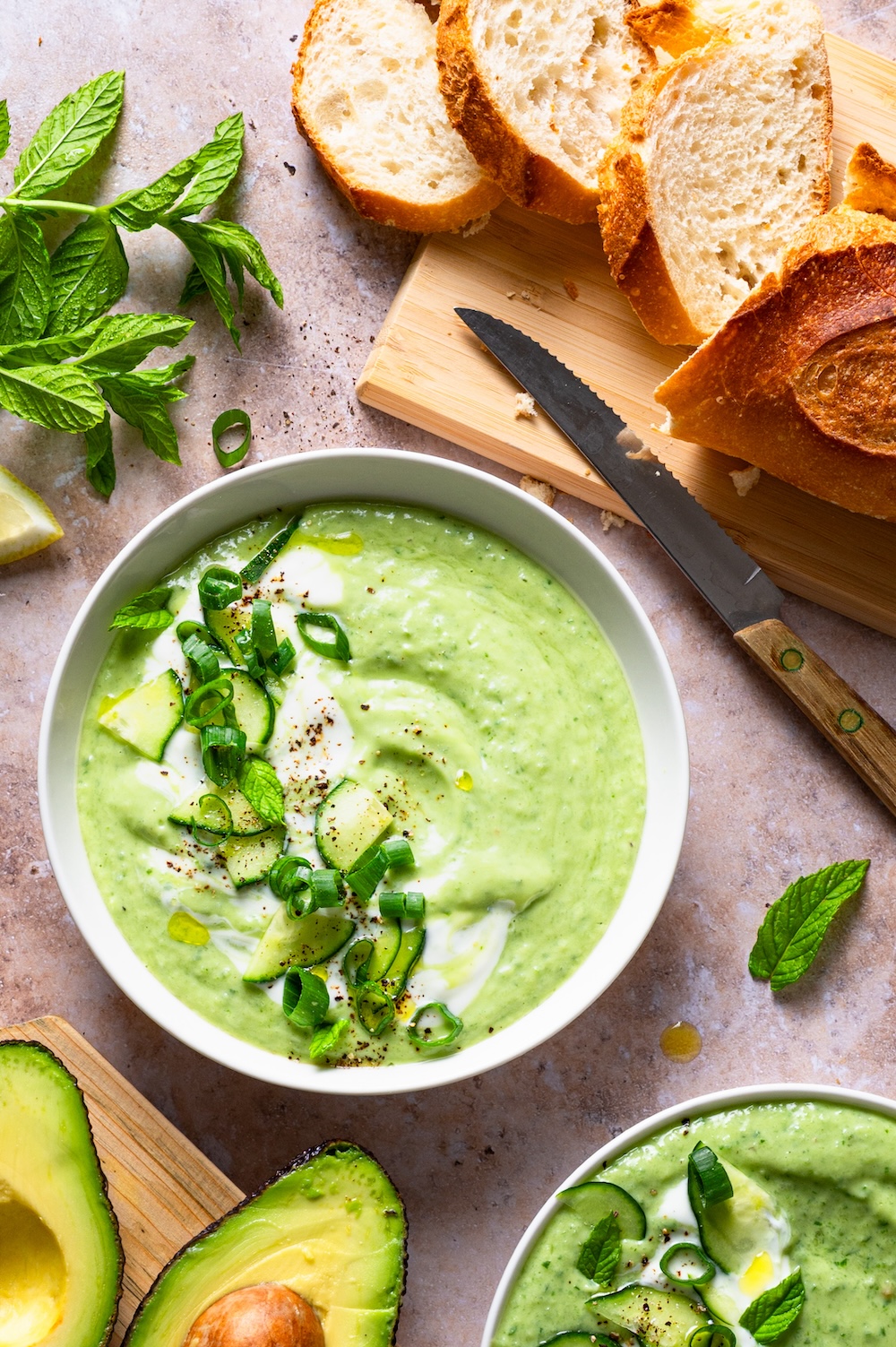 Kalte Suppe mit Gurke, Avocado und Joghurt in einer Schüssel mit Joghurt-Swirls, Gurkenstücken, Frühlingszwiebeln und Minze dekoriert.