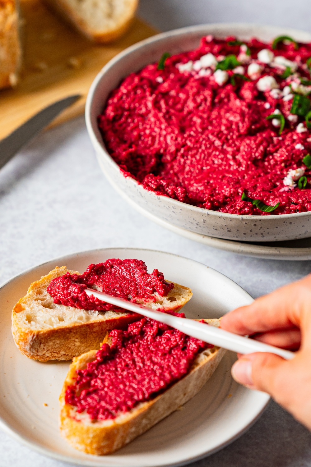 Rote Bete Aufstrich wird auf eine Scheibe Baguette gestrichen.